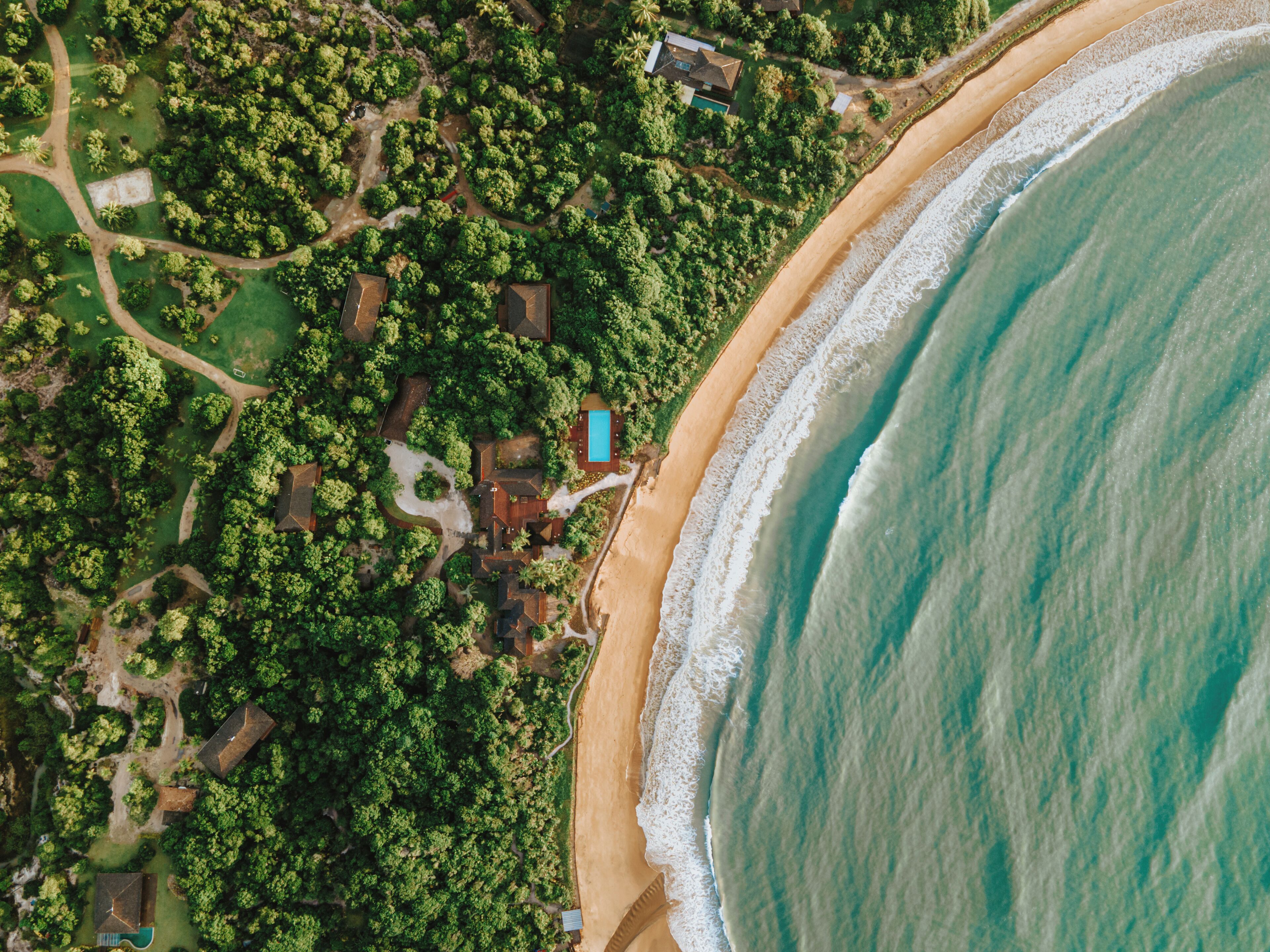 Vue aérienne d’une propriété située sur la côte, avec une plage, une végétation luxuriante et une piscine.