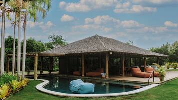 A covered outdoor pool area with a wooden deck, lounge chairs, and a small pool.