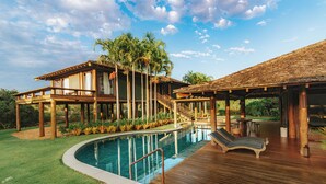 Un resort con piscina, terraza de madera y zona cubierta con sillones de descanso.