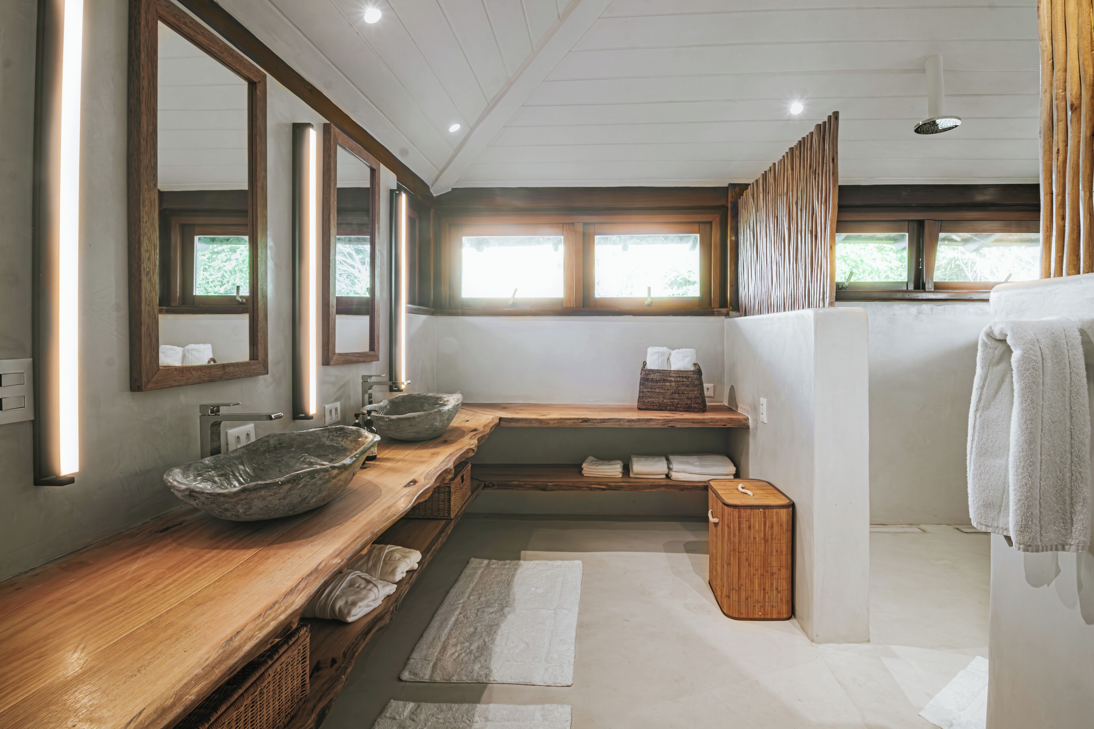 Une salle de bain moderne avec un meuble-lavabo en bois, deux vasques, un grand miroir et une fenêtre laissant entrer la lumière naturelle.