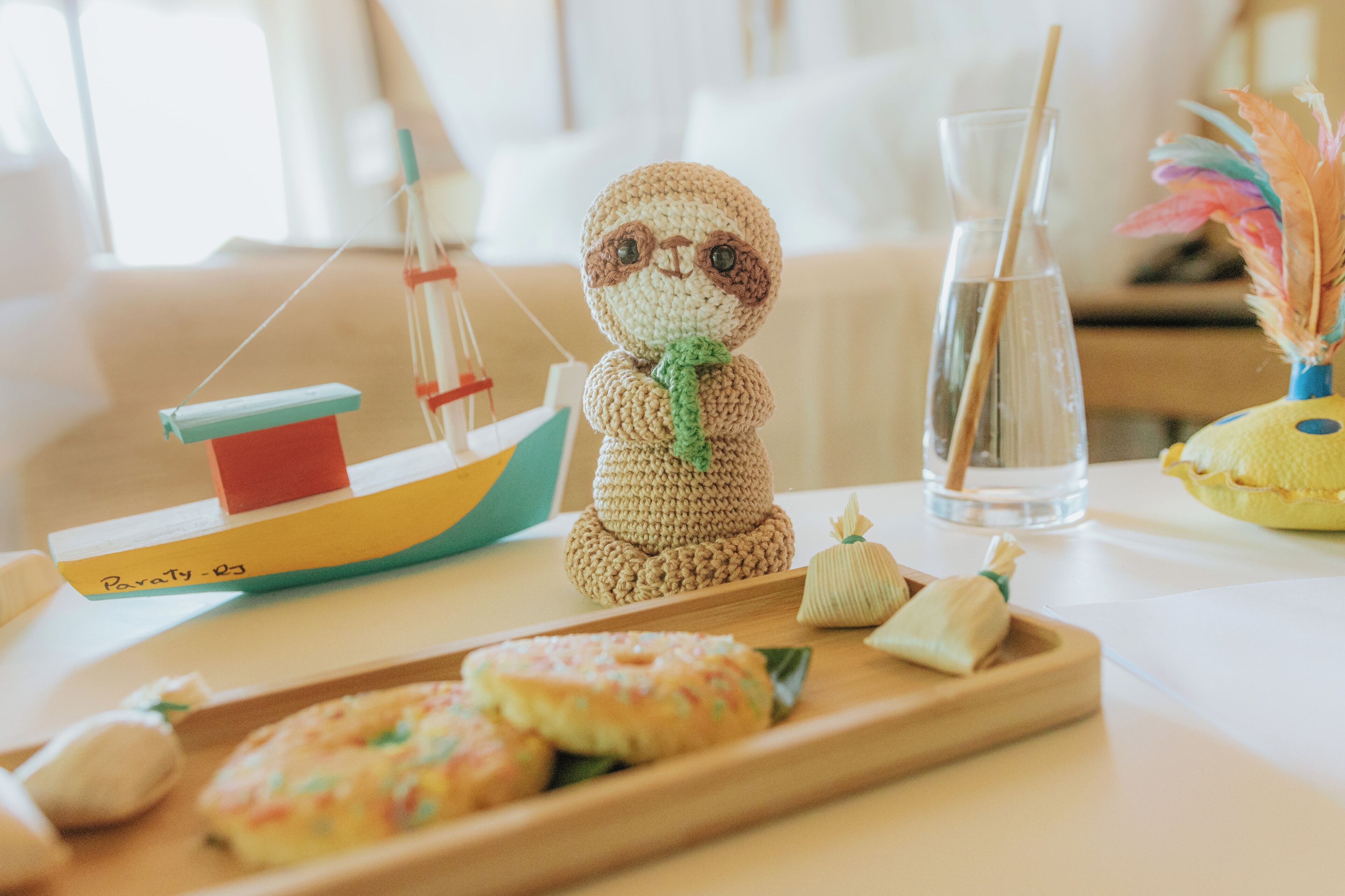 Una figura de ganchillo, un pequeño barco, un vaso con pajita y una bandeja con pasteles.