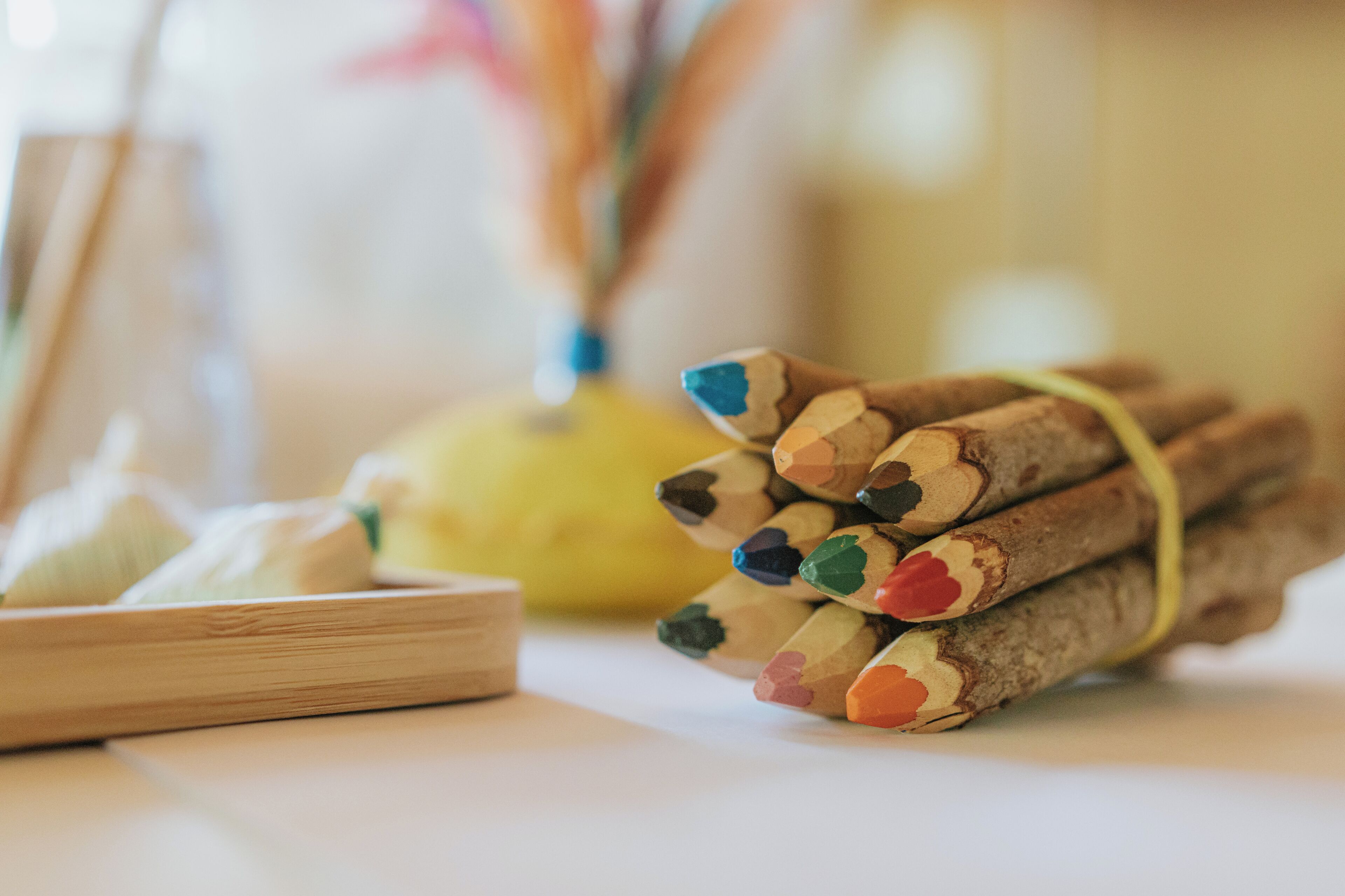 A wooden table with a small bowl of white sugar and a bunch of colored pencils tied together.