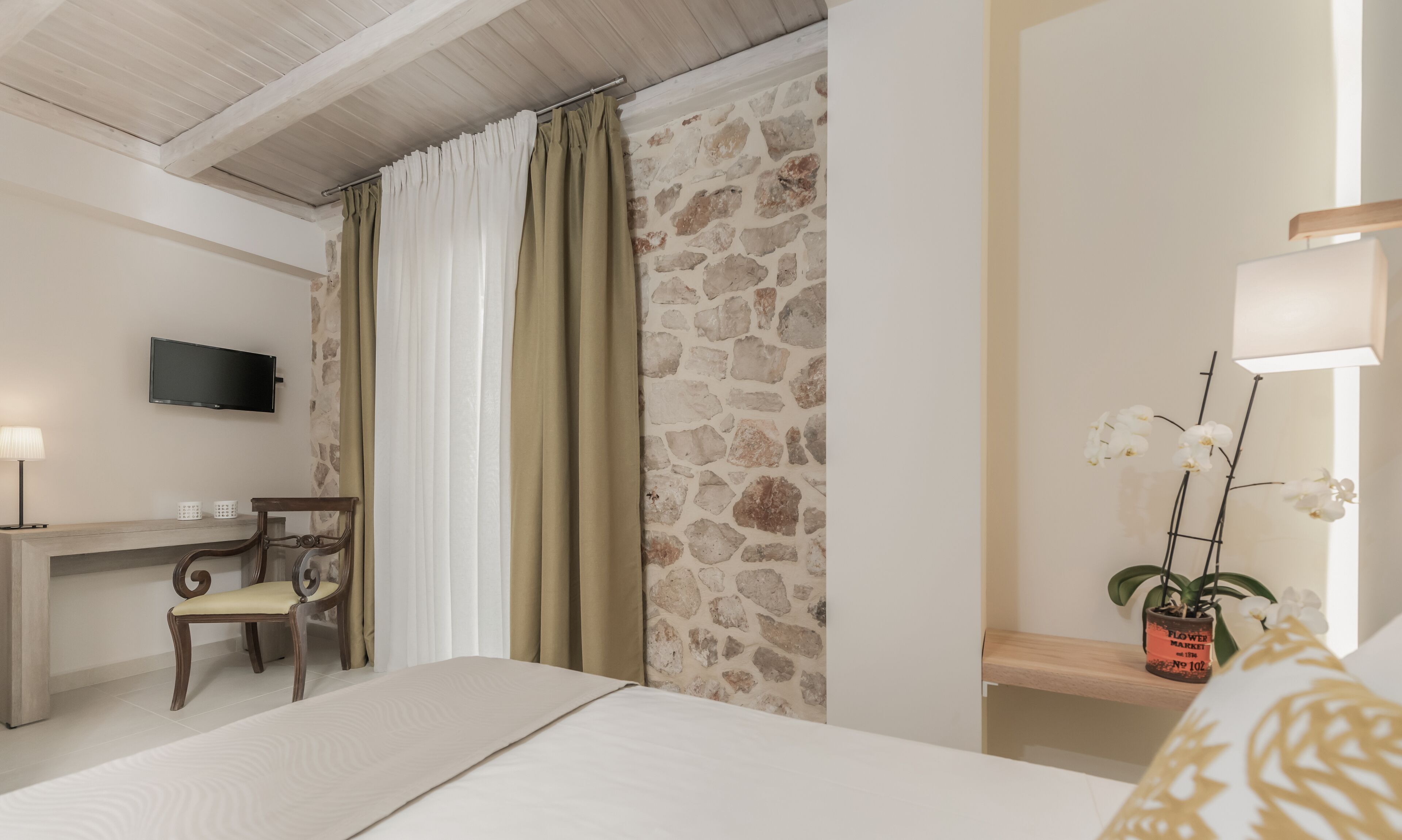 Hotelkamer met een bed, bureau met stoel, televisie, stenen muur en een potorkidee.