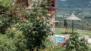A stone building with a tiled roof, a wooden door, and a view of a pool and mountains in the background. - Agrikia Villa (Zakynthos)