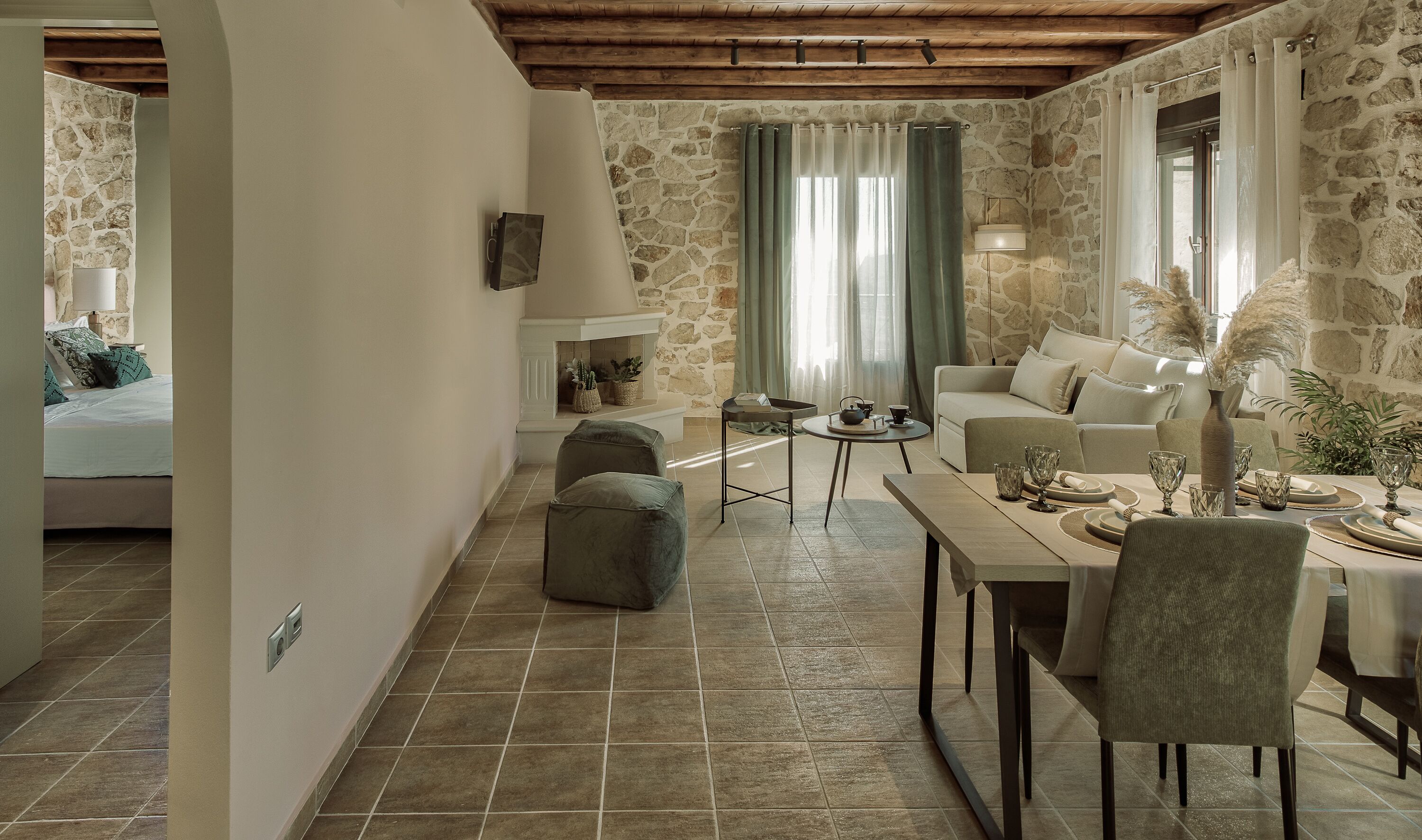 A cozy living room with a stone wall, a sofa, a dining table with chairs, and a small side table with a lamp.