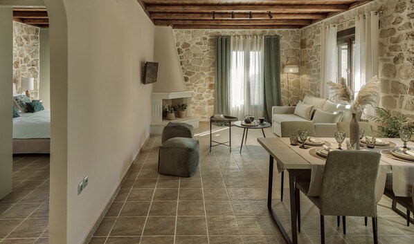A cozy living room with a stone wall, a sofa, a dining table with chairs, and a small side table with a lamp. - Agrikia Villa (Zakynthos)
