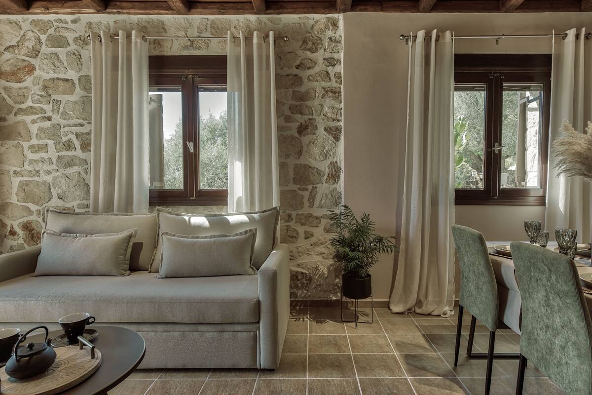 A cozy room with a stone wall, a sofa, a dining table with chairs, and a potted plant.
