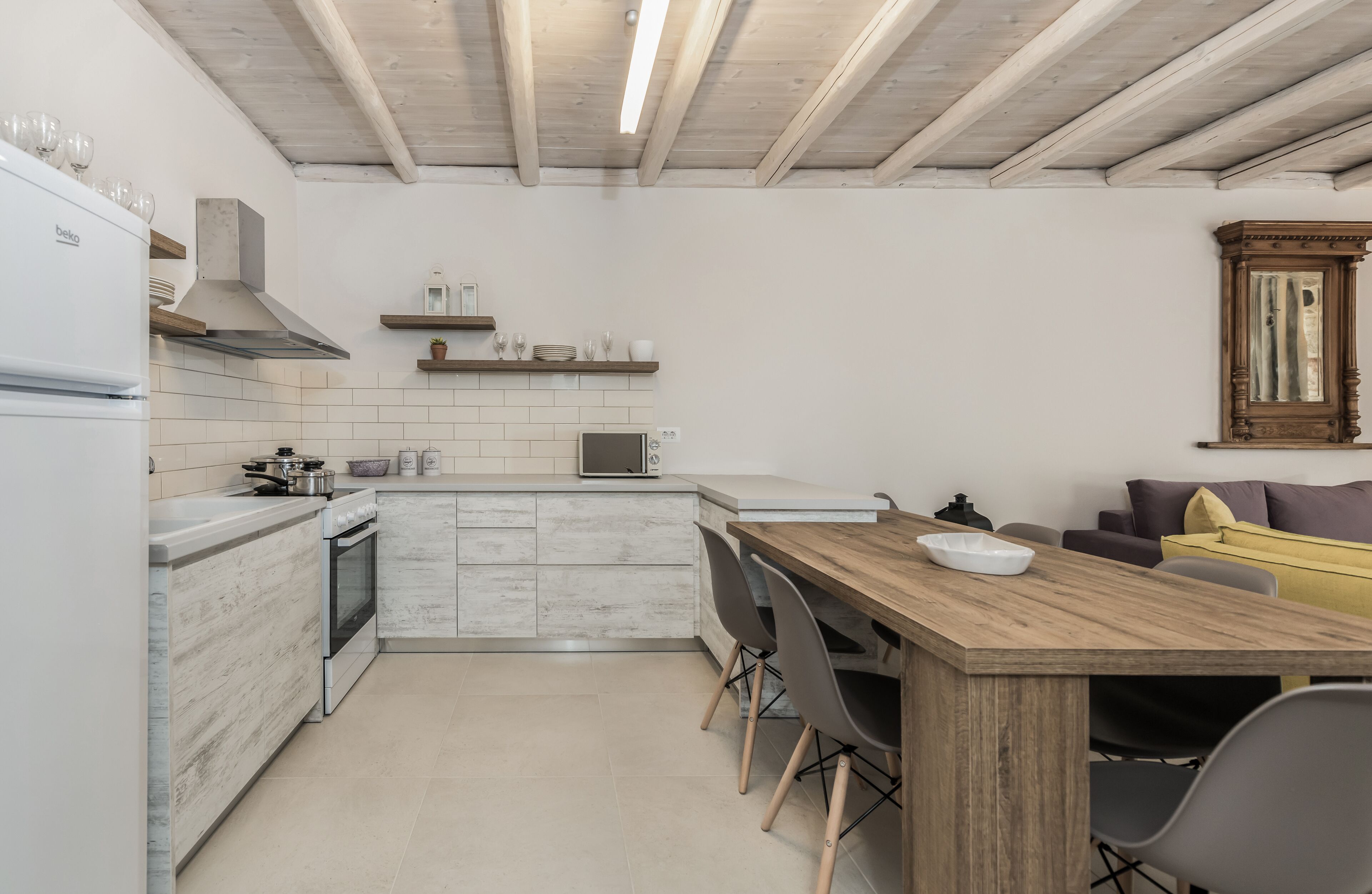 A modern kitchen with white cabinetry, a wooden dining table, and a built-in oven.