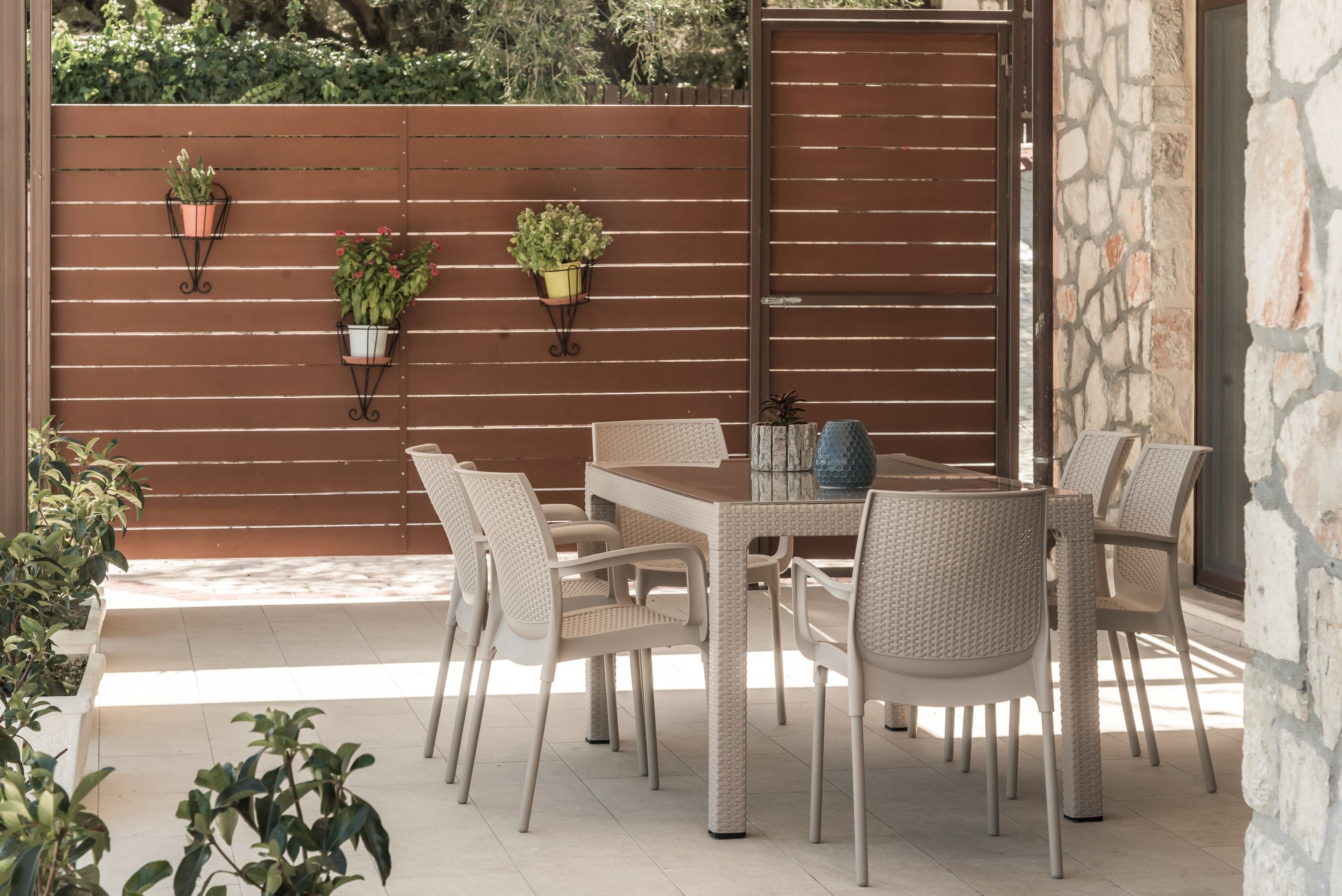 Eine Terrasse im Freien mit Holzlattenzaun, Korbmöbeln und Kübelpflanzen.
