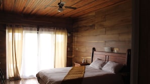 A wooden-paneled room with a bed, a nightstand, and a ceiling fan. - Hotel Bosque Verde Lodge (Sierra)