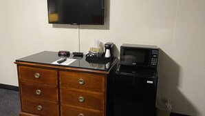 Habitación de hotel con cómoda de madera, televisor de pantalla plana en la pared, cafetera y microondas.