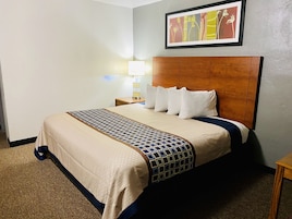 Una habitación de hotel con una cama grande, un cabecero de madera, una mesita de noche con una lámpara y un cuadro en la pared.