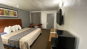 A hotel room with a bed, a desk, a television, and a window with curtains.
