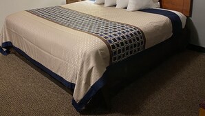 A hotel room with a large bed, a wooden headboard, a framed artwork above the bed, and a nightstand with a lamp.
