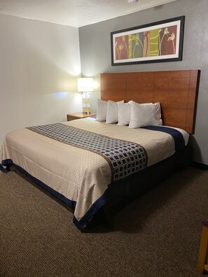 Une chambre d’hôtel avec un grand lit, une tête de lit en bois, une œuvre d’art encadrée au-dessus du lit et une table de chevet avec une lampe.