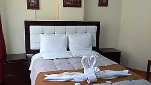 Habitación de hotel con una cama grande, dos mesitas de noche y un cabecero de madera. Hay tres cuadros en la pared.