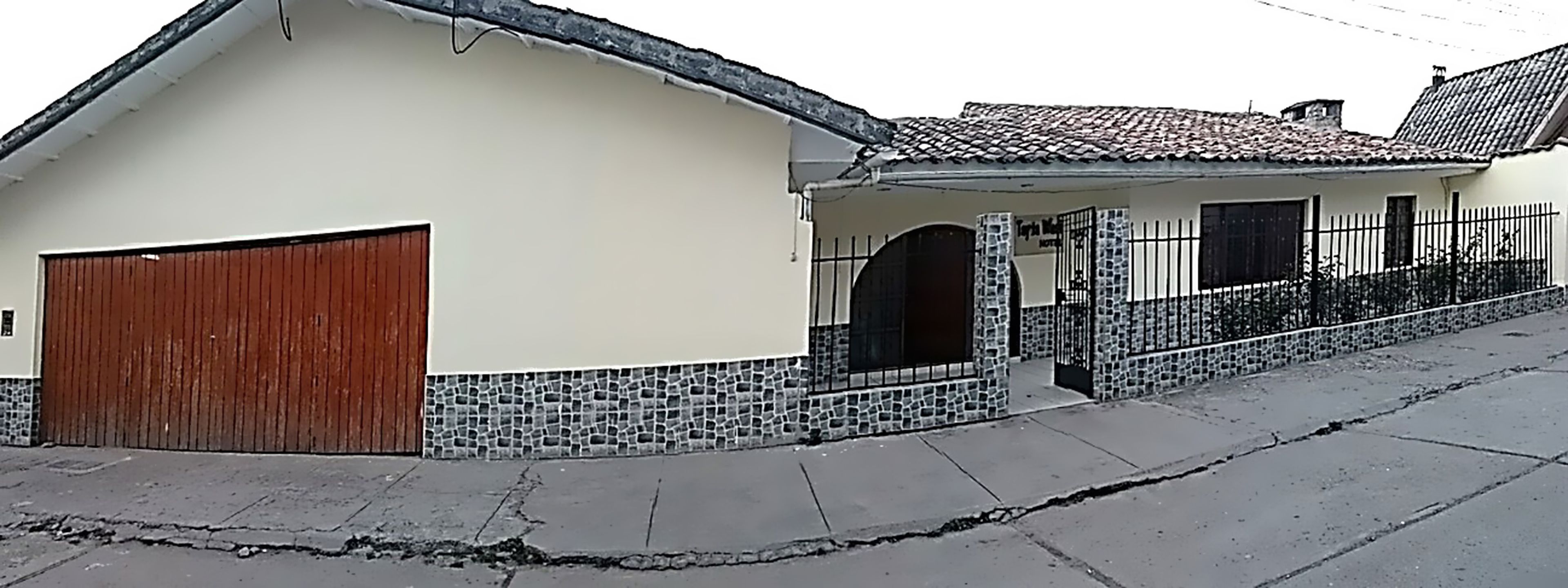 Un bâtiment à deux étages, doté d’un toit recouvert de tuiles, d’une porte de garage en bois et d’une base en pierre.