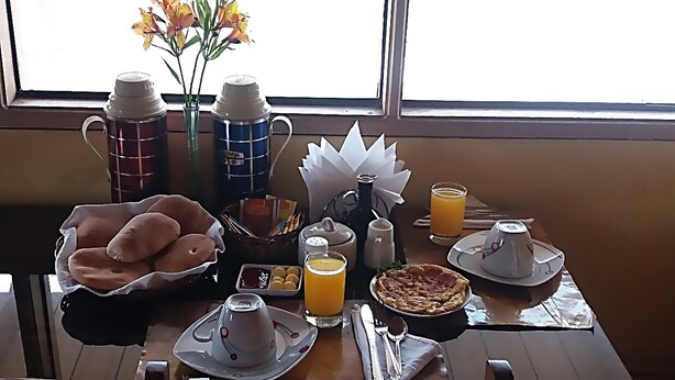 Una mesa cerca de una ventana con una variedad de alimentos, bebidas y condimentos para el desayuno.