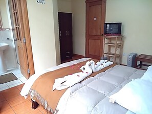Habitación de hotel con cama, televisor sobre un soporte, armario y baño con lavamanos e inodoro.
