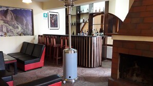 Zona de bar con barra alta, chimenea y asientos con cojines rojos y negros.