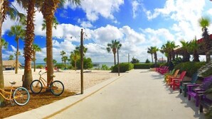 Un paseo marítimo en la playa con bicicletas, sillas de colores y palmeras.