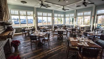 Un restaurante espacioso con numerosas mesas y sillas, ventanas amplias con vistas y ventiladores de techo.