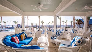 Un espacio lounge al aire libre con mobiliario de mimbre, una piscina y vistas a la playa y el puerto deportivo.