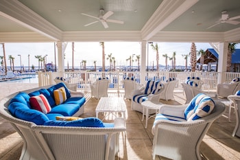 A spacious restaurant with high ceilings, exposed beams, and a brick fireplace. Tables are arranged in a U-shape around the fireplace, with hanging pendant lights above. at The Beach Club at Charleston Harbor Resort and Marina