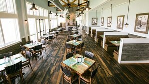 Un restaurante espacioso con techos altos, vigas a la vista y una chimenea de ladrillo. Las mesas están dispuestas en forma de U alrededor de la chimenea, con lámparas colgantes arriba.