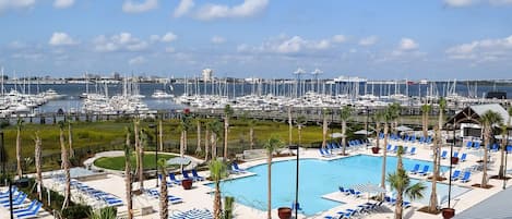 A resort pool area with lounge chairs and palm trees, overlooking a marina with numerous boats.