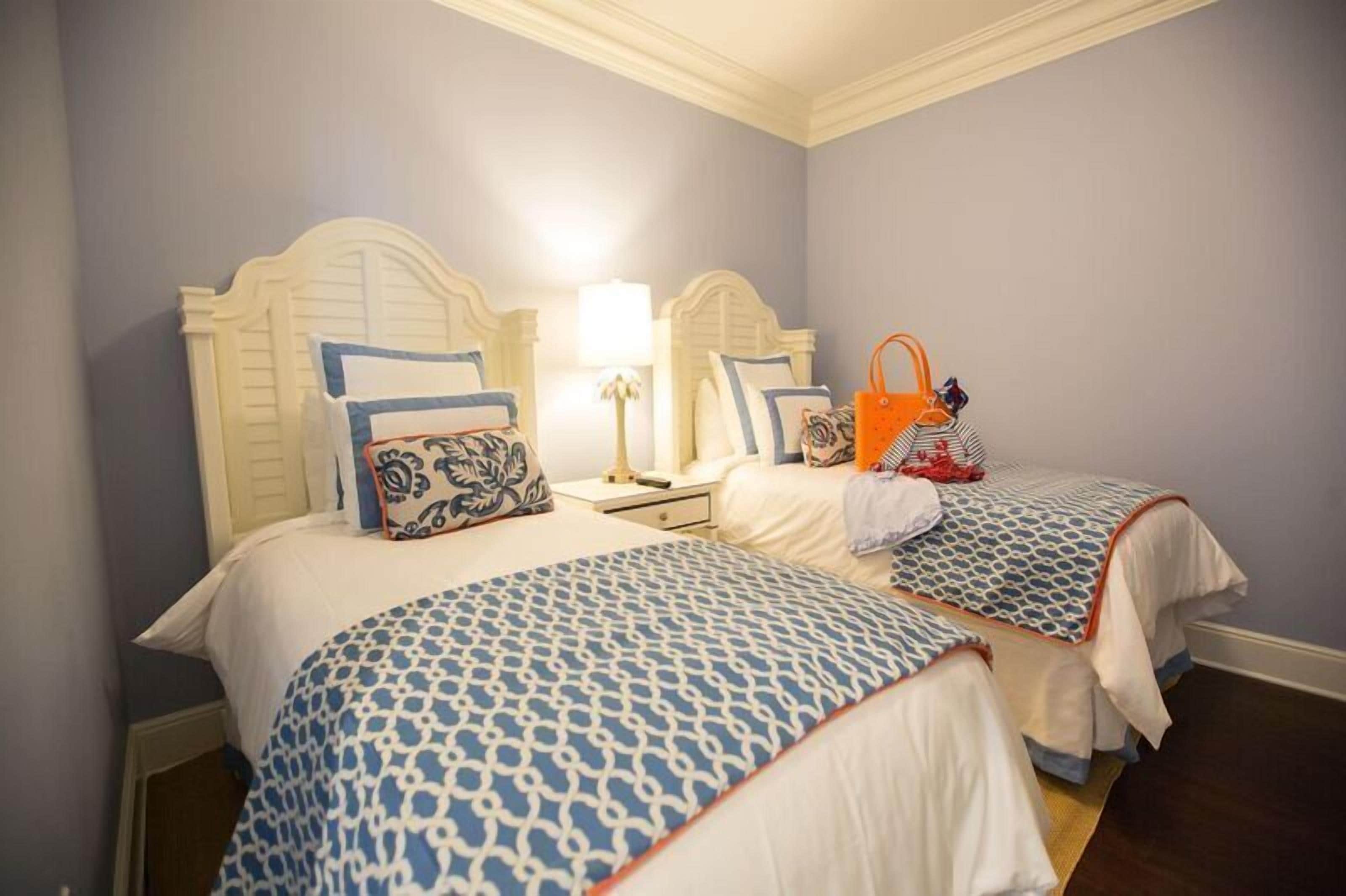 Habitación de hotel con dos camas, cada una con una colcha estampada y almohadas a juego. Se observa un mesita de noche con una lámpara y un bolso encima.