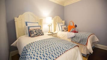 A hotel room with two beds, each with a patterned bedspread and matching pillows. There is a nightstand with a lamp and a handbag on it.