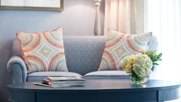 A living room with a grey sofa, patterned cushions, a small round table with books and a vase of flowers.