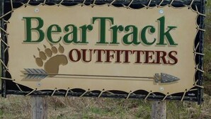 Señal de BearTrack Outfitters con una huella de oso y flechas.