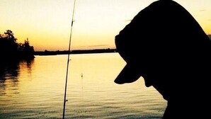 Silueta de una persona con una caña de pescar junto a un cuerpo de agua tranquilo al atardecer.