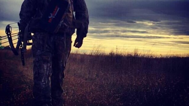 Una persona vestida con indumentaria de camuflaje alejándose de la cámara en un campo bajo un cielo nublado.