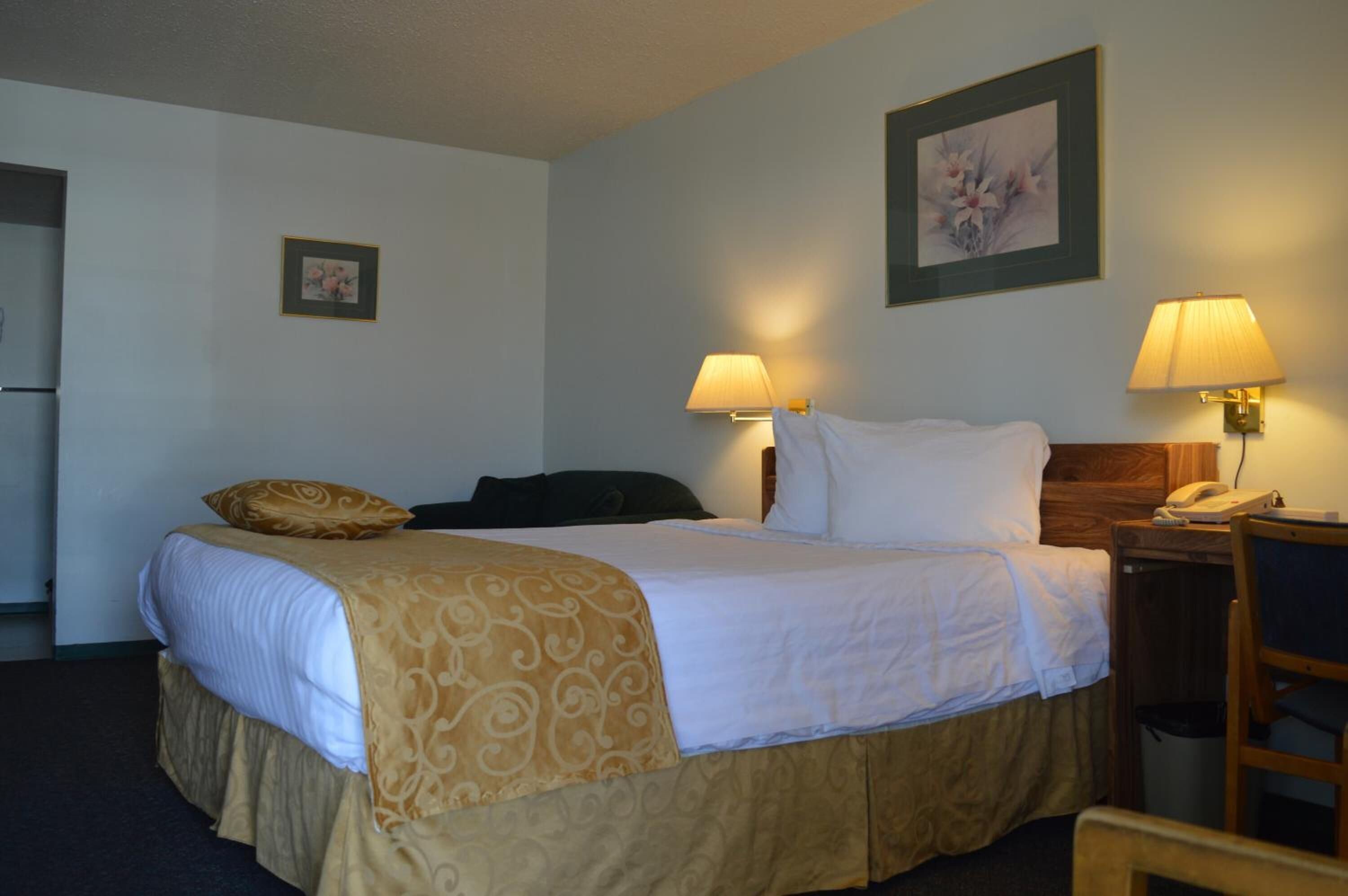 Habitación de hotel con cama, dos lámparas de noche, un teléfono, una silla y un cuadro en la pared.