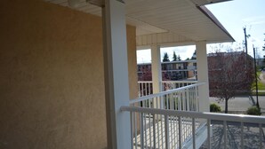 A balcony with a white railing, beige walls, and a view of a parking lot and buildings in the background. - Circle 5 Motel (Olds)
