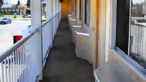 A corridor with a concrete floor, white railings, and orange walls. - Circle 5 Motel (Olds)