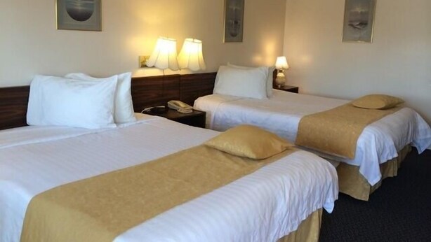 A hotel room with two single beds, each with a headboard, bedside tables, and lamps. - Circle 5 Motel (Olds)