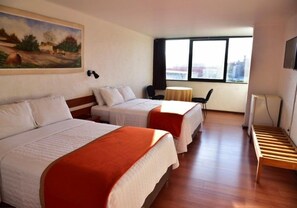 A hotel room with two beds, a small table, a chair, a TV, and a window with a city view.