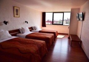 Habitación de hotel con tres camas, televisión y un amplio ventanal.