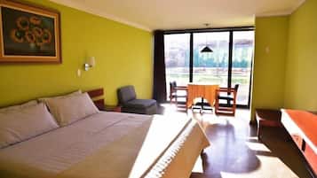 A bedroom with a large bed, a dining table with chairs, and a view through a glass door.