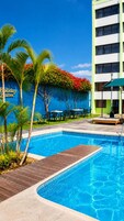 Una piscina con terraza de madera, rodeada de palmeras y un edificio con un letrero que dice 'Holiday Suites'.
