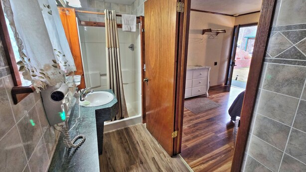 A bathroom with a wooden door, a sink, and a shower. - Cedar Wood Inn (Deadwood)