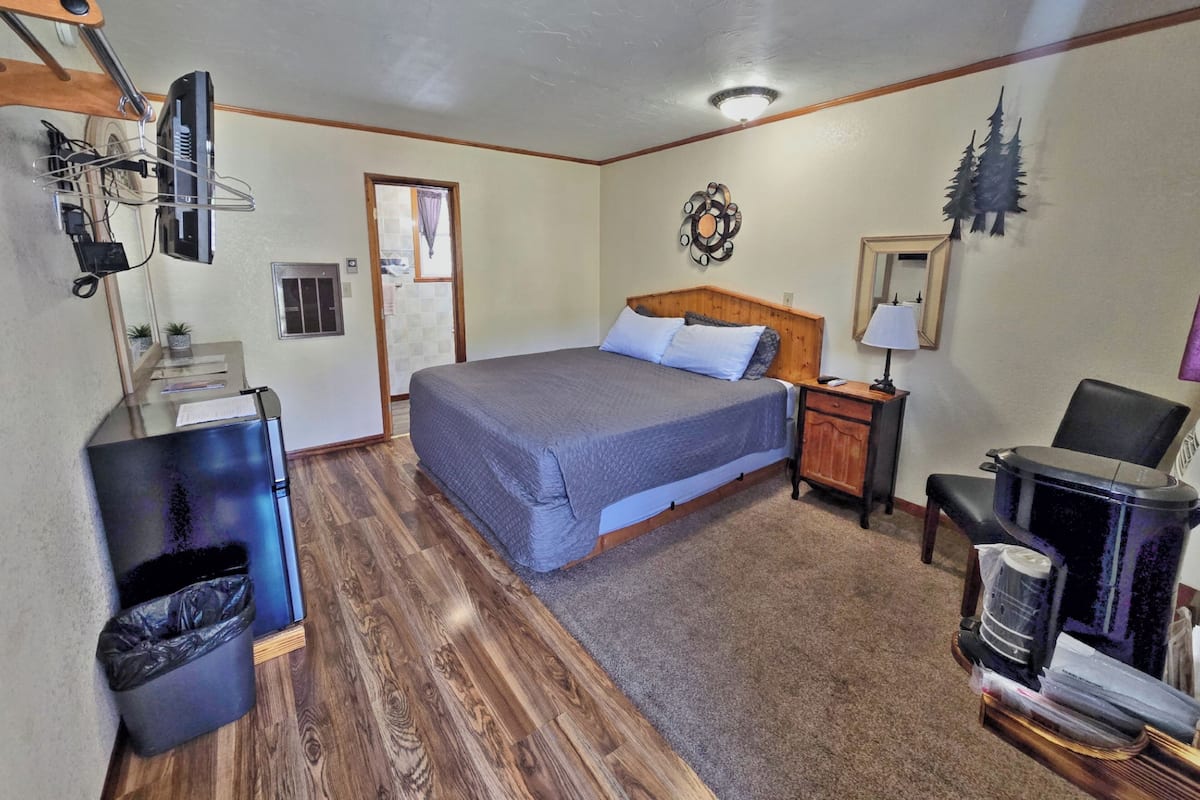 A bedroom with a bed, a nightstand, a chair, a heater, a trash bin, and a wall-mounted shelf.