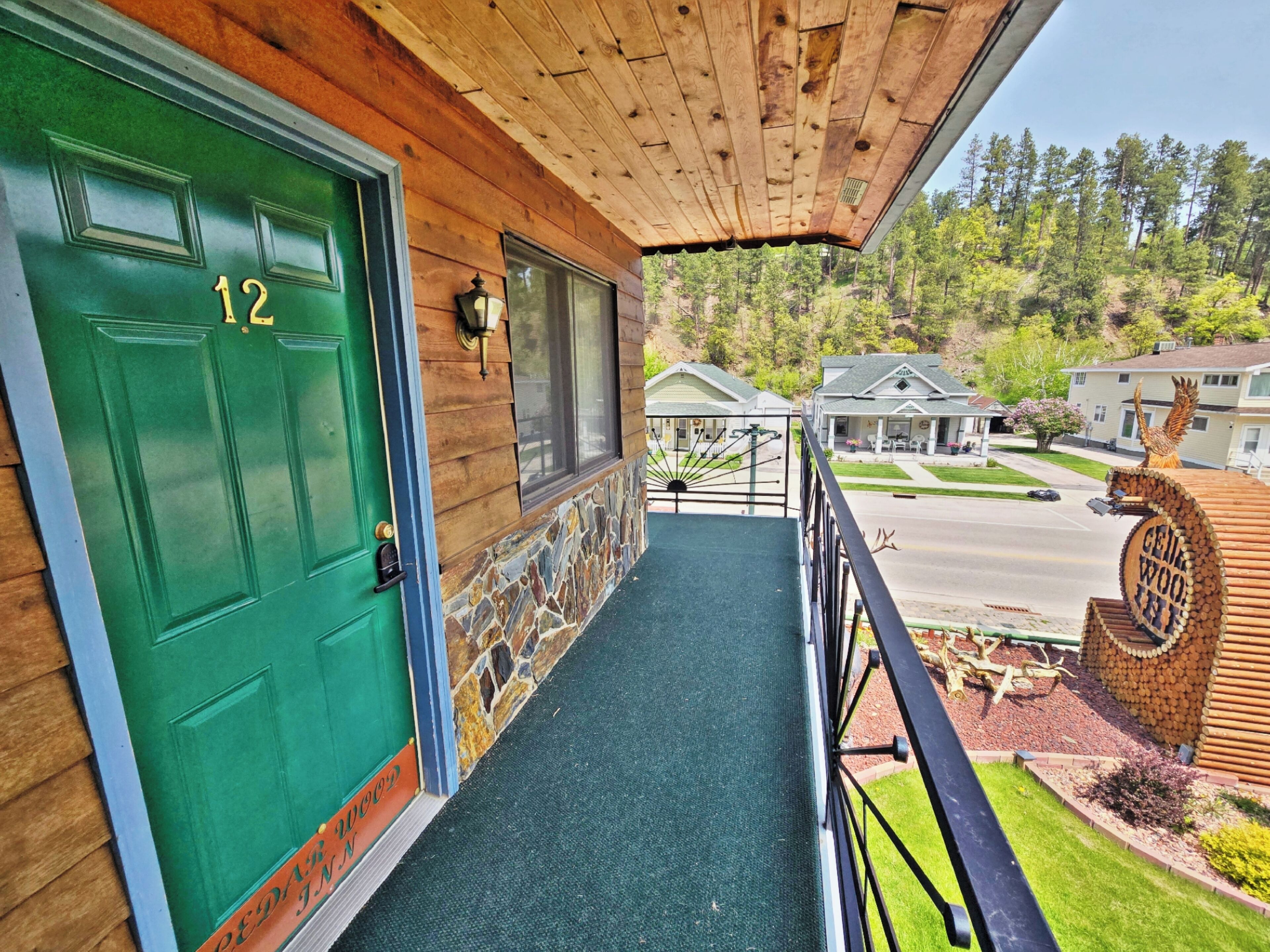 A wooden building with a green door labeled "12" and a stone wall.