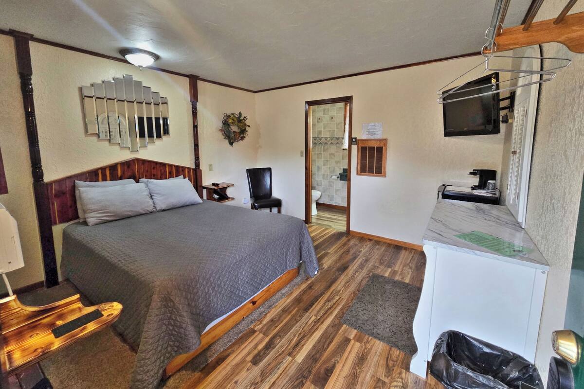 A bedroom with a bed, a chair, a desk, a TV, and a bathroom visible through an open door.