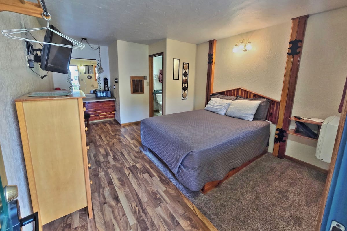 A bedroom with a wooden bed, a desk, a television, and a bathroom visible through an open door.