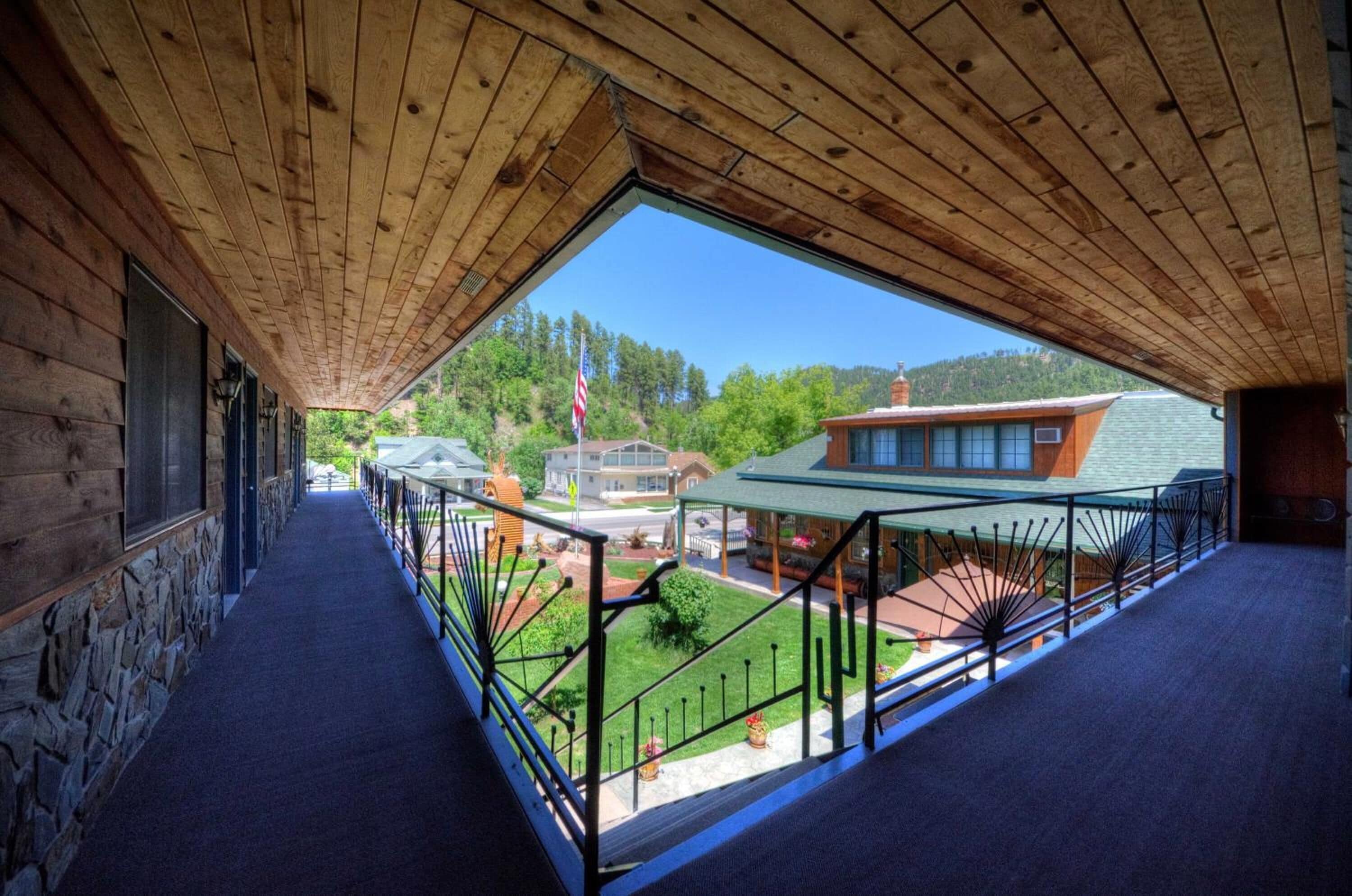 A covered outdoor balcony with a view of a residential area, stone walls, and a clear sky.
